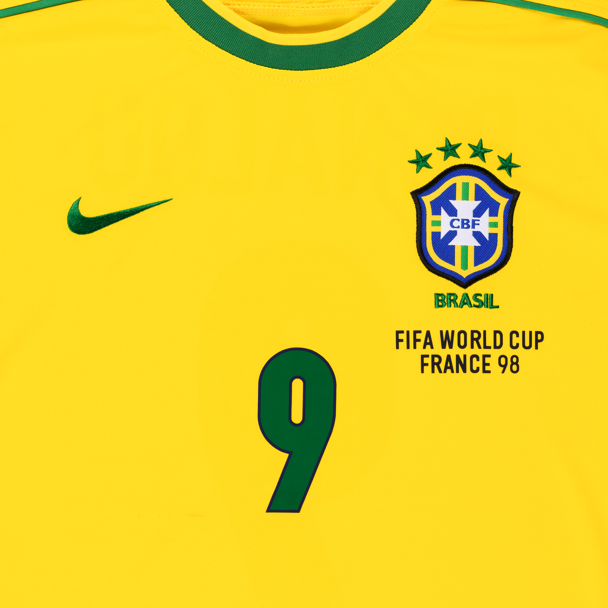 Detailansicht der Vorderseite des gelben Heim-Trikots der brasilianischen Nationalmannschaft zur Fußball-WM 1998 mit Brasilien-Logo, grün gesticktem Schriftzug BRASIL, vier Sternen für vier gewonnene Weltmeisterschaften und der grünen Spielernummer 9 von Ronaldo Luis Nazário de Lima (R9)