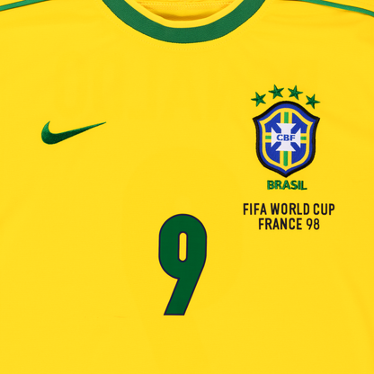 Detailansicht der Vorderseite des gelben Heim-Trikots der brasilianischen Nationalmannschaft zur Fußball-WM 1998 mit Brasilien-Logo, grün gesticktem Schriftzug BRASIL, vier Sternen für vier gewonnene Weltmeisterschaften und der grünen Spielernummer 9 von Ronaldo Luis Nazário de Lima (R9)